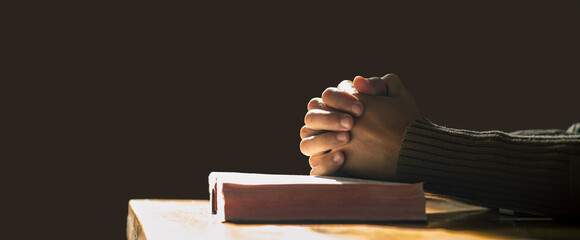 Hands praying of christian put on holy bible with light in morning at wooden table. Close up hands....