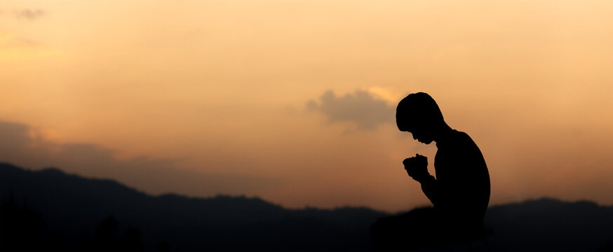 Silhouette of christian kneeling down and praying on mountain at sunset background. Christian concept.