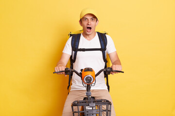 Fast transport express home delivery. Online order. Delivery man in cap with thermo backpack on electric scooter positing isolated on yellow background. - obrazy, fototapety, plakaty