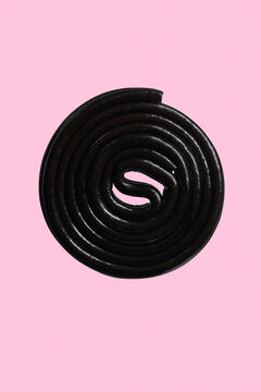 Close up black licorice coil on pink background
