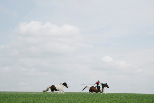 Girl horseback riding, pulling horse on lead in open field
