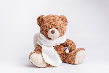 a teddy bear with a thermometer and a knitted scarf is sick on a white background, isolated