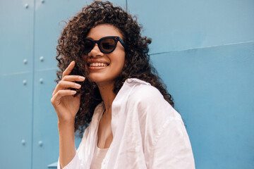 Smiling young african model in stylish sunglasses looking at camera outdoor spring day. Brunette...