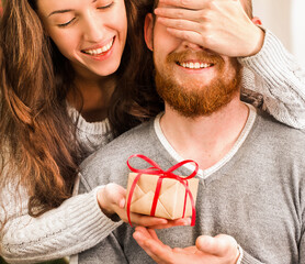 Young happy woman giving a gift to a man, closing his eyes