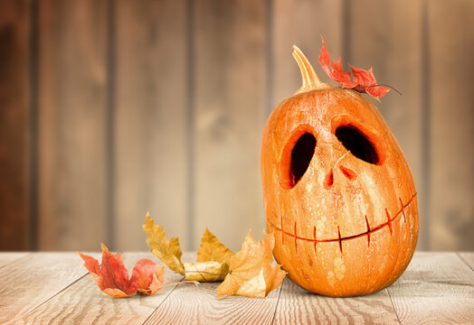 Jack-o-Lantern Pumpkin and autumn leaves on wooden background