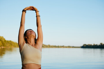 A middle-aged woman is relaxing on the dock and doing yoga breathing exercises.