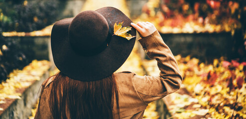 Back view of beautiful young woman in the hats standing at the autumn street. Trendy young red hair woman in fall in park. Concept of autumn mood.