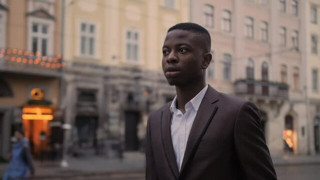 Portrait of handsome african man in stylish suit posing on street of city. Young businessman standing outdoors and looking aside.