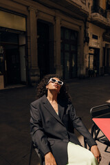 Nice young african girl with stylish sunglasses sitting on chair in cafe enjoying sunshine outdoor....