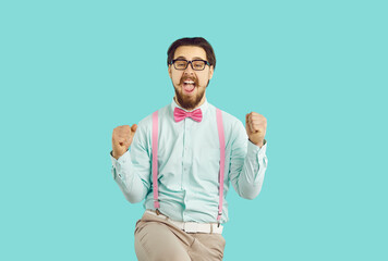 Cheerful happy male hipster nerd rejoices in his success standing on light blue background. Guy with mustache and beard wearing shirt, suspenders and glasses happily clenched his fists shouting YES. - obrazy, fototapety, plakaty