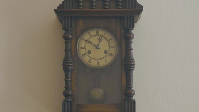 Antique grandfather clock hanging on a wall of a rose-colored house. Vintage object of grandparents or ancestors