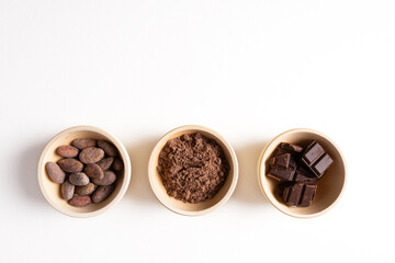 Cocoa beans, ground cocoa and chocolate in wooden plates on a white background