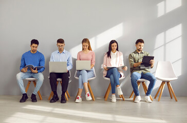 Group of young people sitting along the wall in an office corridor, waiting for job interviews or...