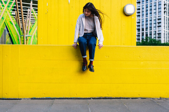 Young woman sitting on yellow wall