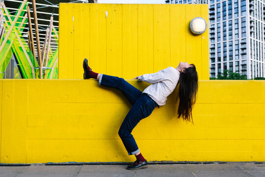 Young woman leaning backwards standing on one leg by wall