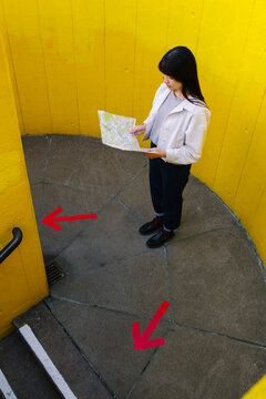 Young woman looking at map standing by arrow symbols