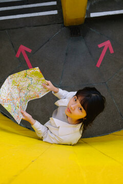 Young woman holding map standing by wall with arrow symbols on floor