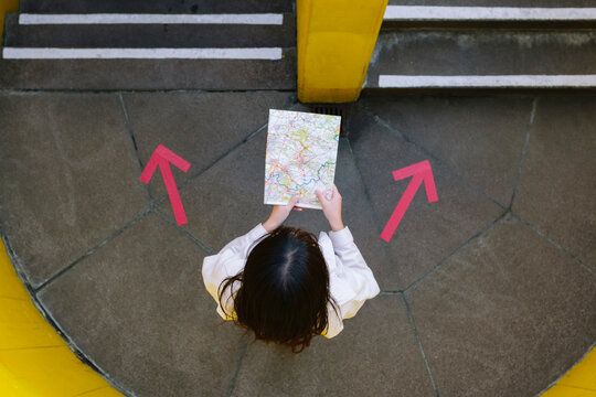 Young woman reading map standing amidst arrow symbols
