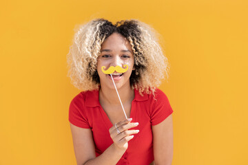 Happy woman with mustache prop in front of yellow wall