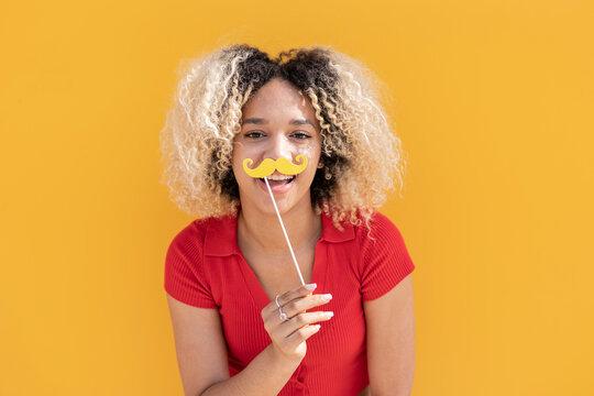 Happy woman with mustache prop in front of yellow wall
