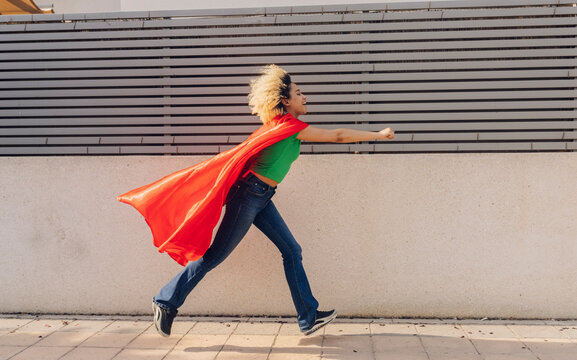 Smiling young woman wearing cape running on footpath