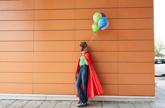 Woman wearing crocodile mask leaning with multi colored balloons on wall