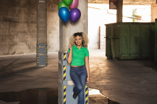 Young woman with multi colored balloons leaning on column in parking garage