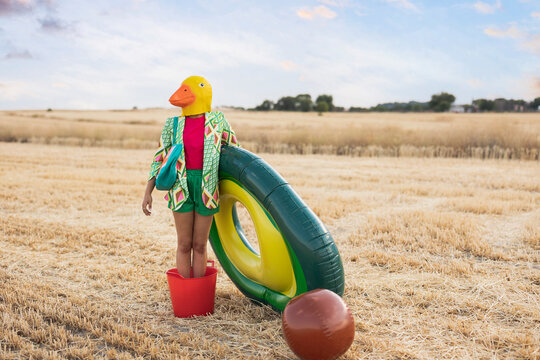 Woman wearing duck mask standing in bucket with inflatable ring at field