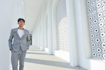 Full body business man standing in front of a white building. Wearing a gray suit ,shirt ,gray pants 