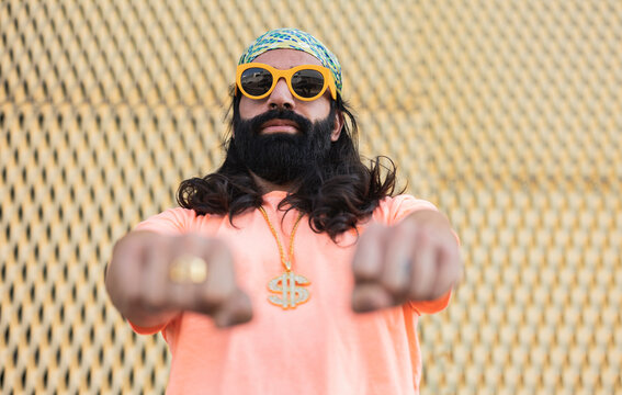 Bearded man wearing sunglasses gesturing fists in front of wall