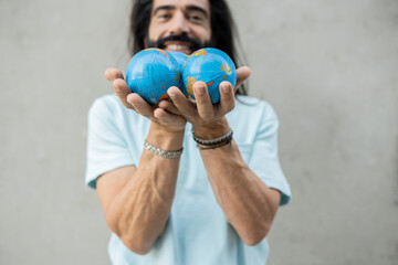 Smiling man with hands cupped holding toy globes in front of wall