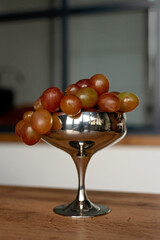 A bunch of red ripe juicy grapes in a metal bowl on a wooden table. Food, healthy eating. Soft selective focus.