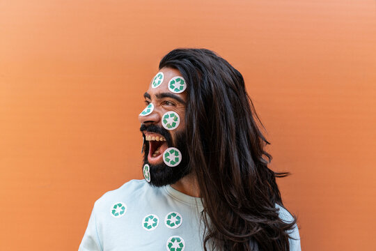 Shouting Bearded Man With Recycling Stickers On Face In Front Of Wall