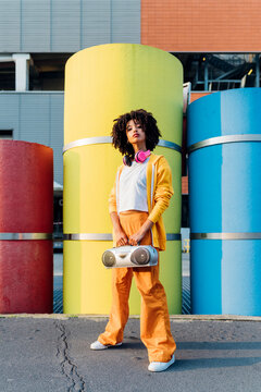 Young woman holding boom box standing in front of colorful pipes