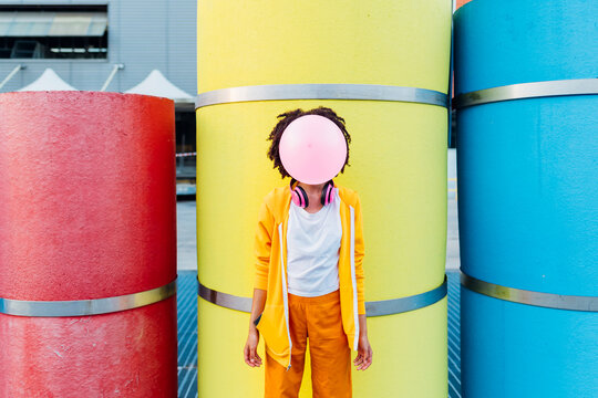 Young woman blowing bubblegum in front of colorful pipes