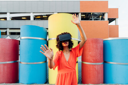 Young woman wearing virtual reality simulator gesturing in front of colorful pipe