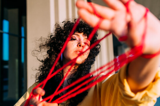Young woman playing cats cradle with thread on sunny day