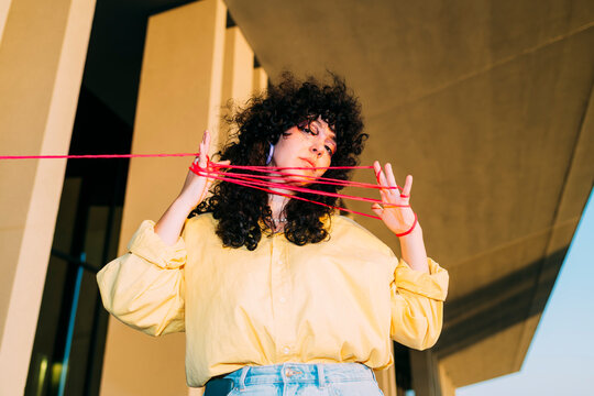Curly hair woman playing cats cradle with thread