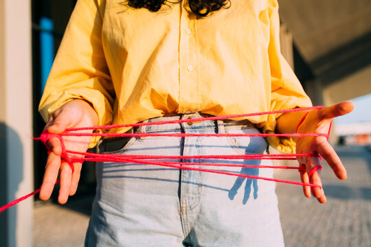 Woman playing cats cradle with thread on footpath