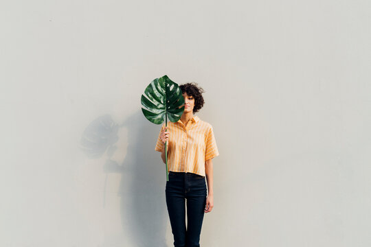 Woman holding monstera leaf standing in front of wall