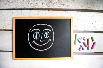 There is a black board on the table and a cheerful face and a pile of chalk are drawn on it with chalk