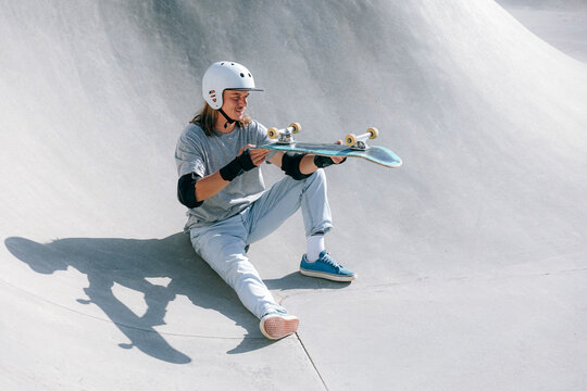 Man with helmet checking skateboard in skate park - Powered by Adobe
