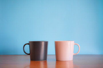 Black and Pink ceramic coffee cup on wood desk with blue background. 
