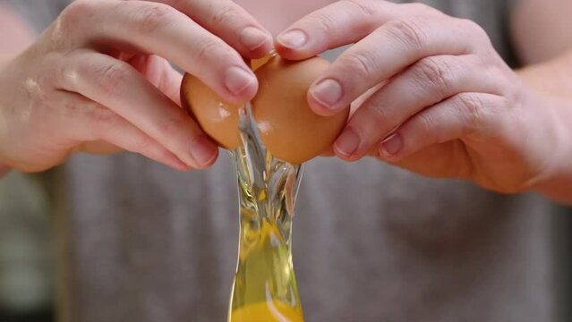 Fresh brown egg being cracked in slow motion yolk falls out of frame