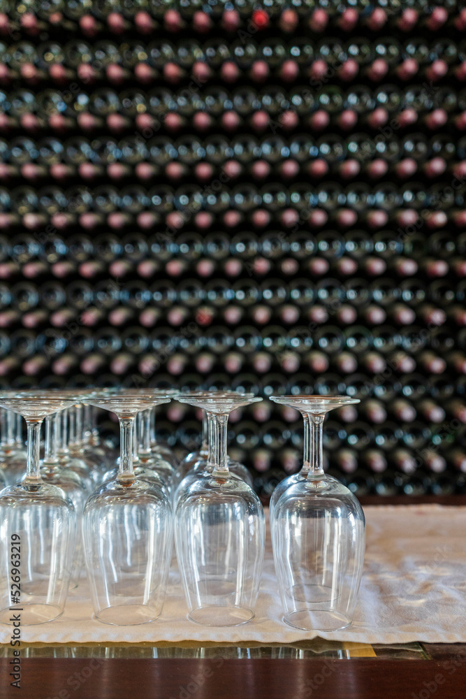 Wall mural Empty wine glasses with many  stacked bottles as a background - preparation to wine tasting in winery, Lanzarote, Spain