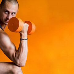 photo of a strong and athletic man holding an orange dumbbell in his hand orange background