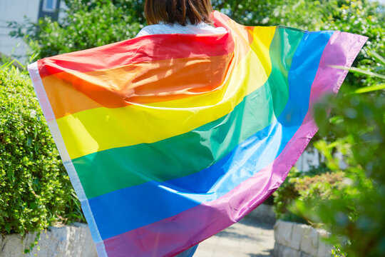 LGBTQイメージ　外で虹色の旗を羽織る女性の後ろ姿