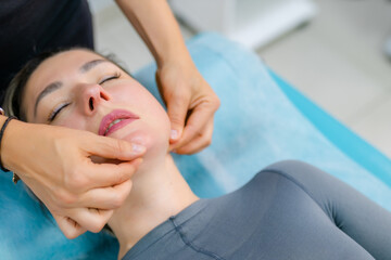 Fototapeta na wymiar unidentified young woman masseur doing facial massage to young client woman