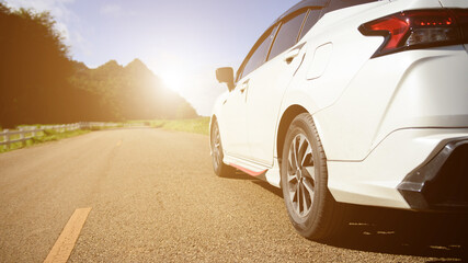 Close-up rear view of a white car with morning light with mountains and sky on the road.
