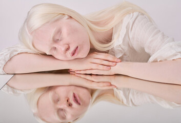 Portrait of albino girl with white hair and eyelashes posing with her eyes closes against white...